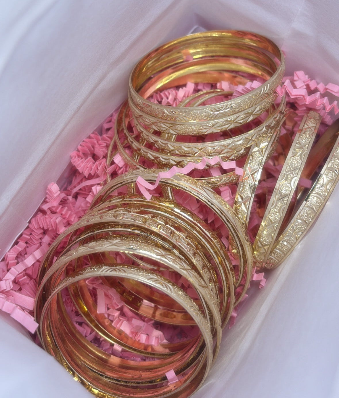 Gold bangles in a box with pink crinkle paper
